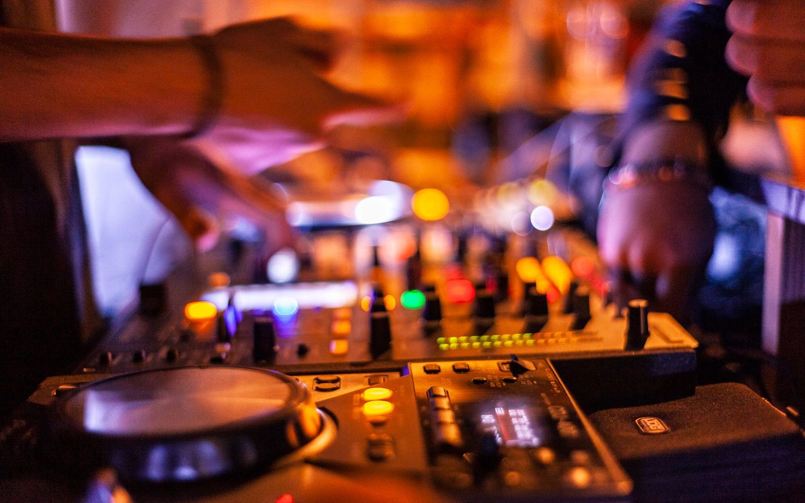 A DJ's hands working a glowing club mixer under warm amber light